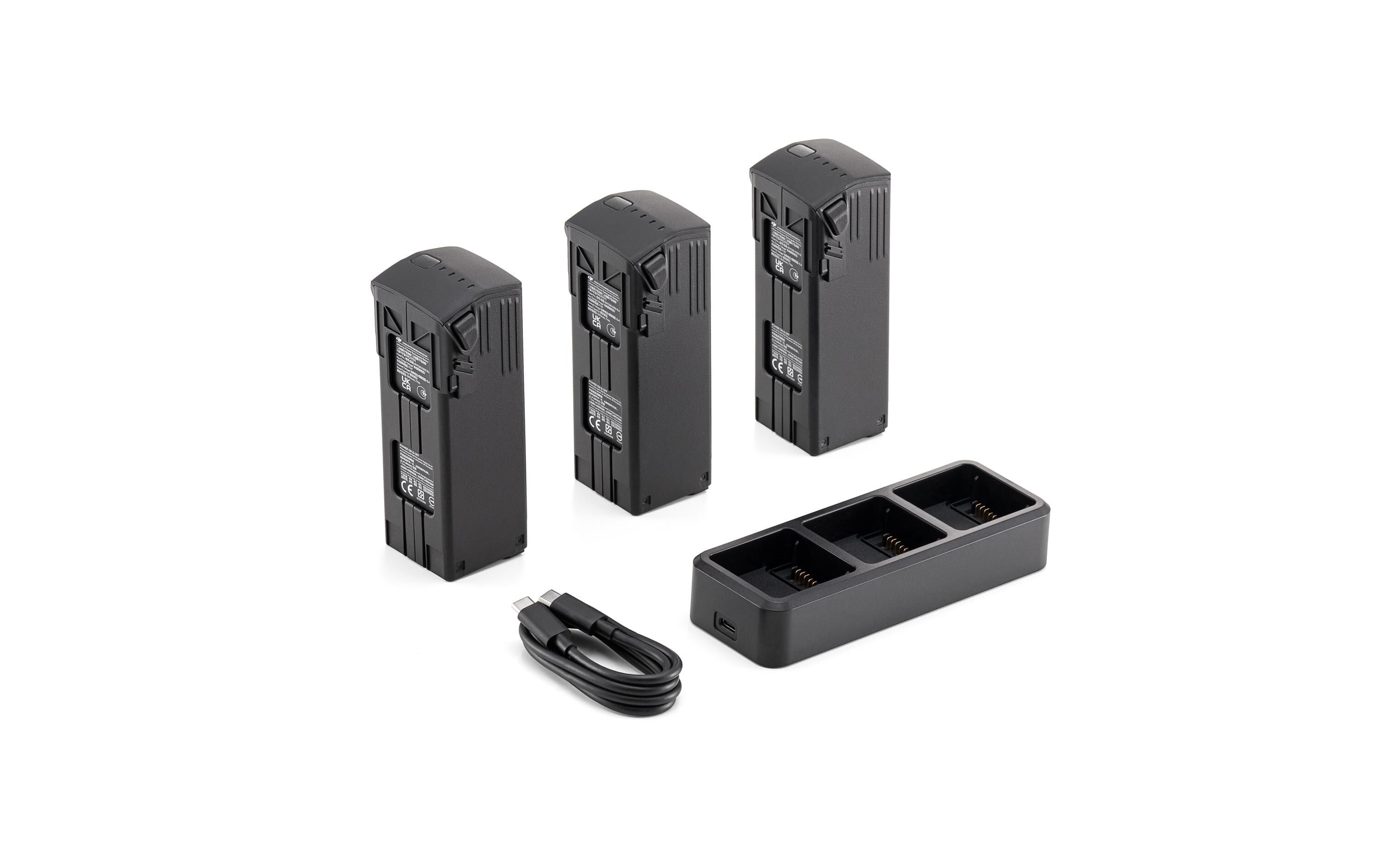 Drei schwarze Kamera-Akkus stehen aufrecht neben einer dreifachen Akku-Ladestation und einem USB-Ladekabel, alles auf weißem Hintergrund.
