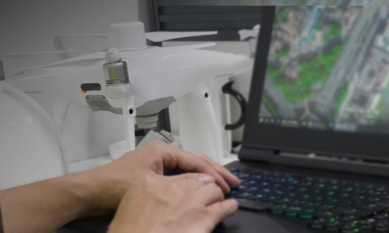 Eine Person arbeitet an einem Laptop, der eine Luftbildkarte mit DJI Terra: Hochmoderne 3D Modellierungssoftware für Präzise Luftbildvermessung und Kartierung von DJI Enterprise zeigt, während im Hintergrund eine weiße Drohne auf dem Schreibtisch steht.
