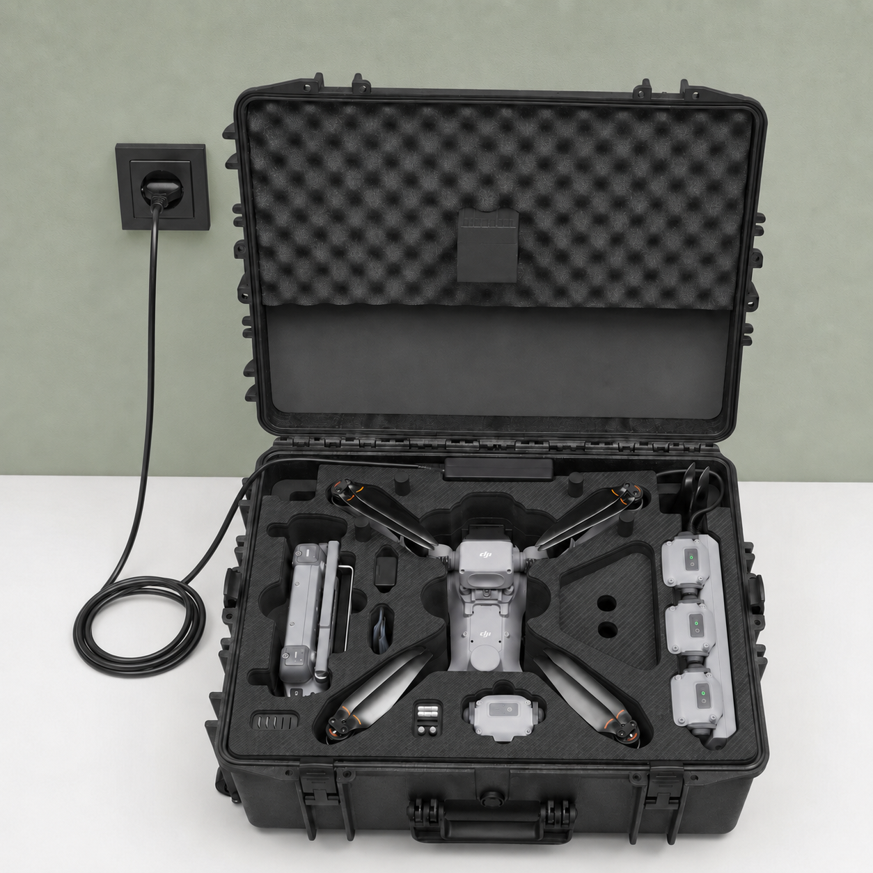 Ein schwarzer TomCase XT620 „Ready to Fly / Ready to Charge“-Outdoor-Koffer für DJI Matrice 4D / 4TD mit Schaumstofffächern bietet sicheren Platz für eine Quadcopter-Drohne, drei Akkus, einen Controller und Zubehör. Das TomCase steht auf einer weißen Fläche in der Nähe einer Steckdose, an die ein Netzkabel angeschlossen ist, sodass alles direkt im Koffer aufgeladen werden kann.
