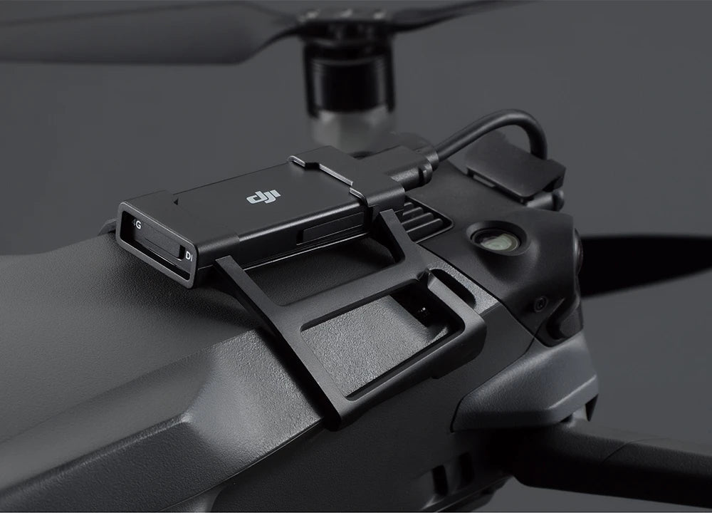 Eine Nahaufnahme einer DJI Mavic 3-Drohne mit dem DJI Enterprise DJI Mavic 3 Series Dongle Mount Kit von DJI Enterprise, mit einem sichtbaren Propeller und Logo auf dem Modul vor einem dunklen Hintergrund.