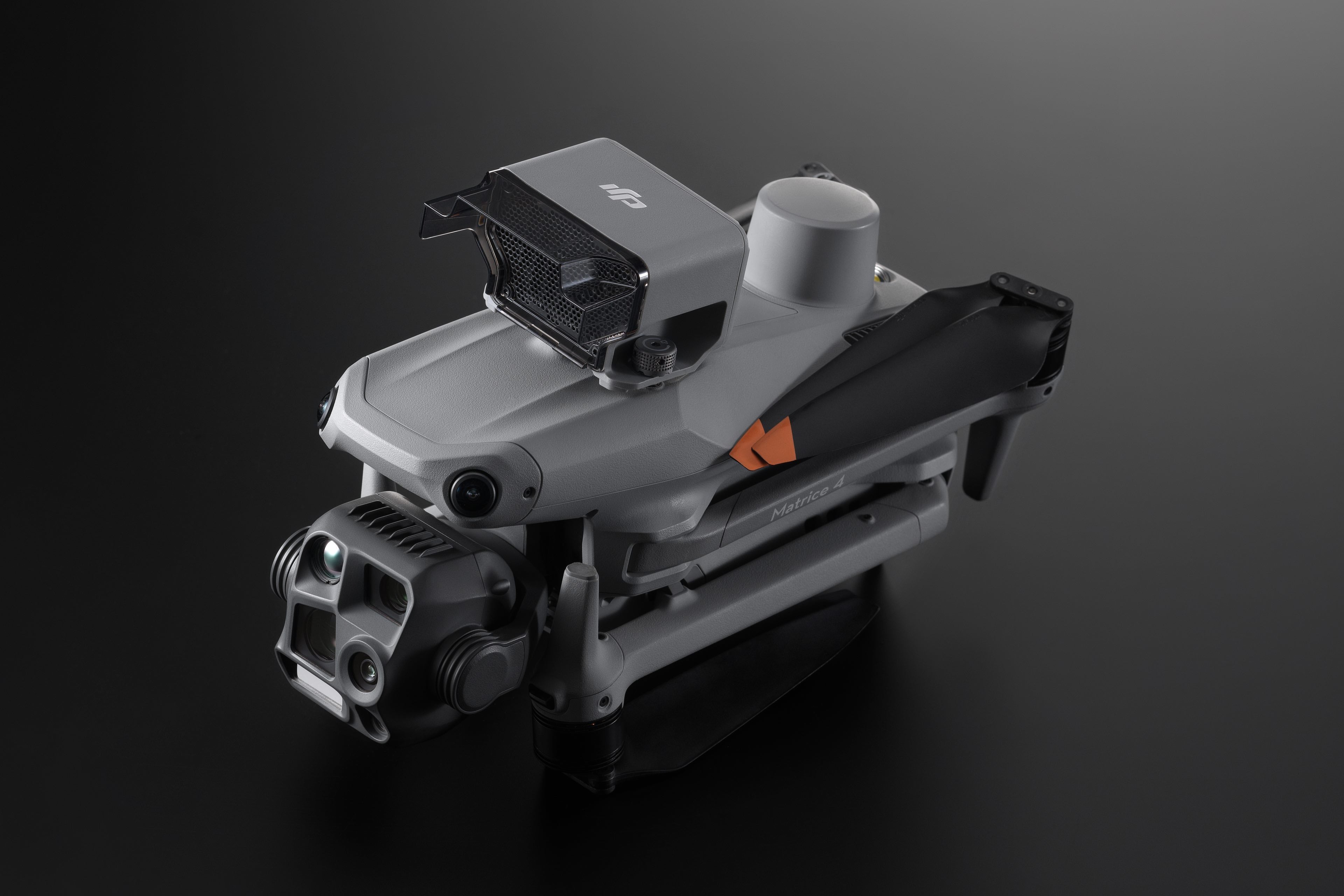 Eine Drohne der DJI Enterprise Matrice 4-Serie mit elegantem Metalldesign steht vor einem dunklen Hintergrund. Sie verfügt über gefaltete Arme, ein markantes Kamerasystem für Echtzeitübertragung, ein glattes, modernes Finish und ist mit dem DJI AS1-Lautsprecher ausgestattet. Ein kleines Logo ziert die Oberseite.