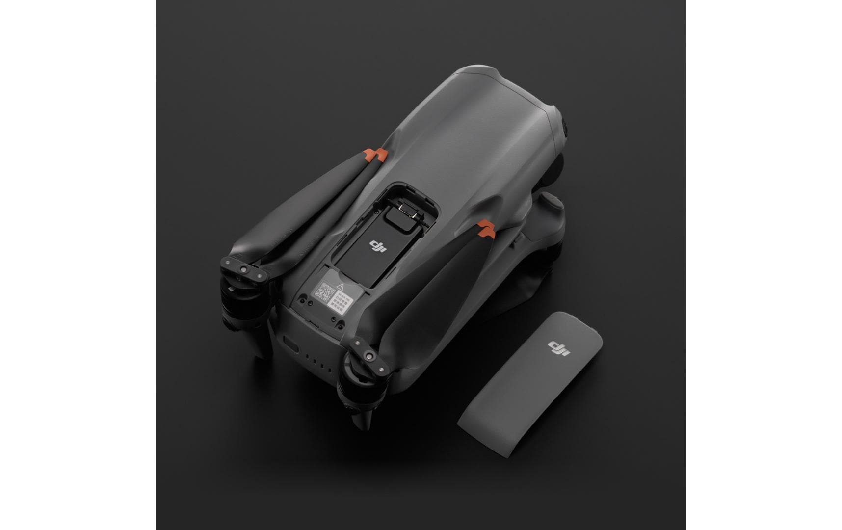 Eine DJI Enterprise DJI Mini 4 Pro Drohne mit elegantem, dunkelgrauem Finish steht auf einer schwarzen Oberfläche neben einem passenden grauen Akkupack. Dezente orangefarbene Akzente in der Nähe der Propeller deuten darauf hin, dass sie in Verbindung mit dem DJI Cellular Dongle 2 atemberaubende Luftaufnahmen über 4G-Netze machen kann.