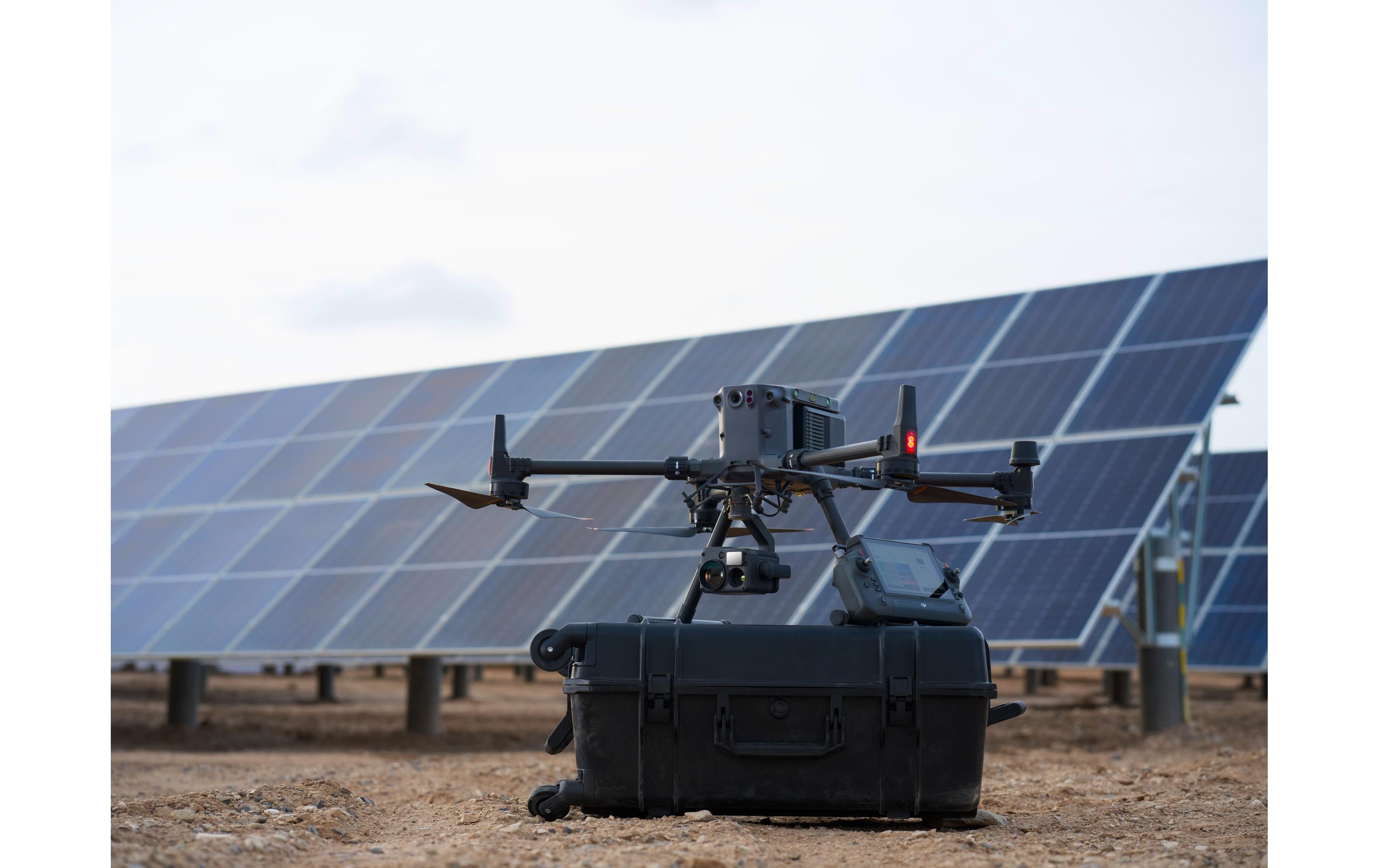 Ein DJI Enterprise Multikopter Matrice 350 RTK (EU) mit DJI Care Basic ruht auf seinem Hartschalenkoffer und ist bereit, atemberaubende Luftaufnahmen vor großen Solarmodulen im Freien zu machen.