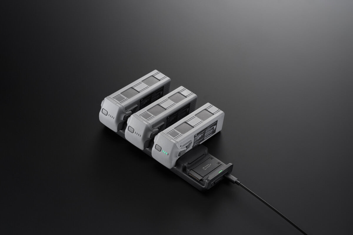 Vier graue DJI Matrice 4 Intelligent Flight Batteries liegen ordentlich auf einer dunklen Oberfläche. Ein Akku ist an einen DJI Enterprise Matrice 4 Series Charging Hub angeschlossen. Die kleine grüne Anzeige zeigt die volle Ladung an und sorgt so für einen übersichtlichen Aufbau.