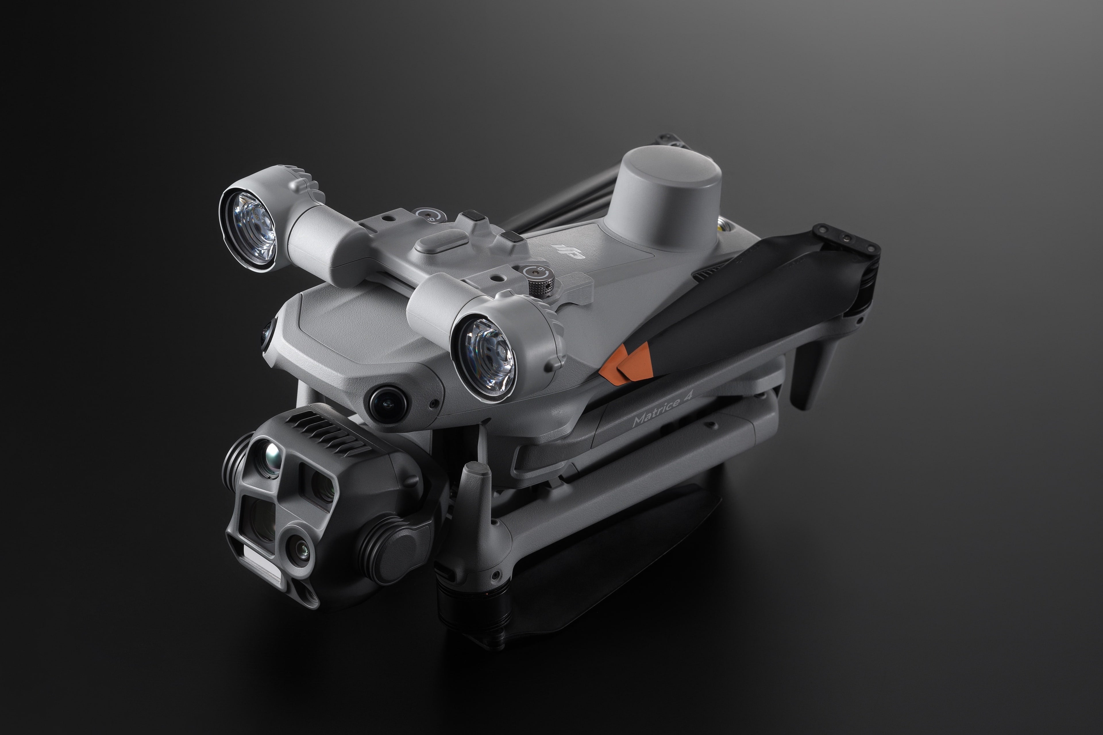 Eine schlanke, kompakte Drohne mit zwei Frontlichtern ruht auf einer dunklen Oberfläche. Sie verfügt über eine eingebaute Kamera und den DJI AL1 Scheinwerfer – Spotlight für die M4 Serie (M4E, M4T). Der Markenname „DJI Enterprise“ ist deutlich sichtbar und sorgt für einen beeindruckenden Look.