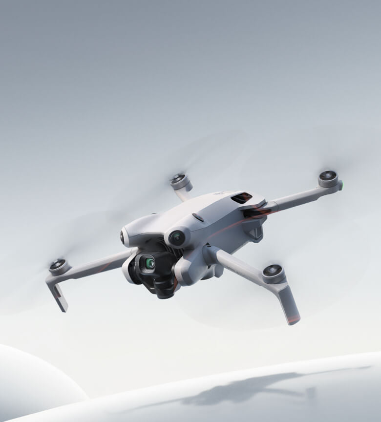 Eine schlanke DJI Mini 4 Pro Fly More Combo (RC 2) von DJI Consumer schwebt vor einem grauen Himmel. Sie bietet mit ihrer kardanisch aufgehängten Kamera eine außergewöhnliche Bildgebungsleistung und besticht durch ihr stromlinienförmiges, kantiges Design.
