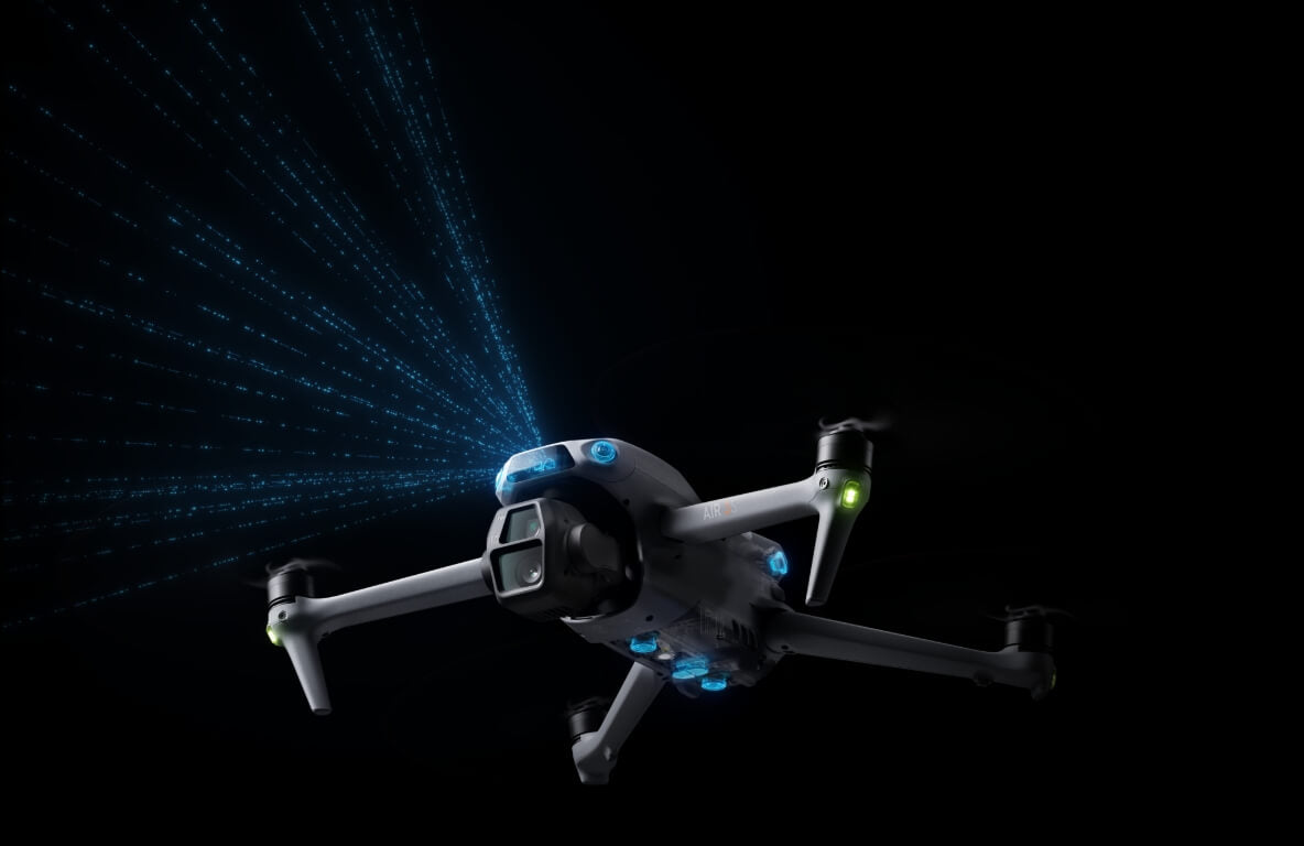 Die DJI Air 3S Fly More Combo (RC 2) von DJI Consumer, eine weiße Drohne mit Dual-Kamerasystem, gleitet elegant durch die Dunkelheit. Ausgestattet mit vier Propellern projiziert sie einen blauen Lichtfächer aus mehreren LEDs sowie kleine gelbe und grüne Lichter und bietet eine beeindruckende Flugzeit von 45 Minuten.