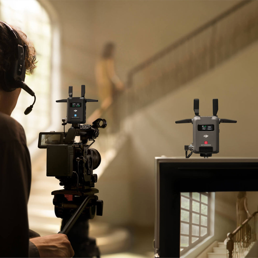 Eine Person mit Headset bedient eine Videokamera mit dem DJI Pro Digitale Bildübertragung RX – DJI SDR Transmission Receiver (Reichweite bis zu 3 km) mit sichtbarer drahtloser 1080p-FHD-Videoausrüstung im Innenbereich und filmt eine verschwommene Gestalt auf einer Treppe.