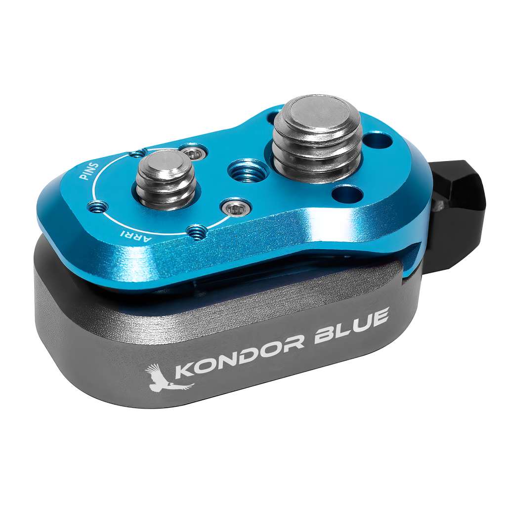 Eine Nahaufnahme eines blau-grauen Kamerazubehörs mit zwei silbernen Knöpfen oben zeigt die Marke Kondor Blue und ein eingraviertes Vogellogo. Es scheint sich um das Mini-Schnellverschlusssystem – Mini Lock Quick Release Plate – zu handeln, Teil des Kamera-Rig-Systems von Kondor Blue für schnelle Konnektivität.