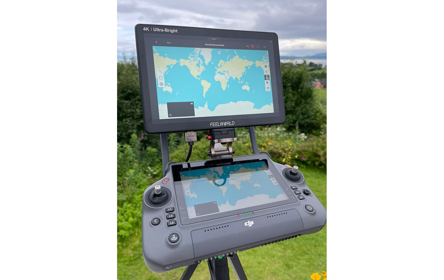 Ein 4K-Bildschirm mit einer Weltkarte ist mithilfe der LifThor RC PLUS Utility Mount II auf einem DJI Enterprise RC Plus-Controller montiert und auf einem Stativ vor Gras und Wolken aufgestellt.