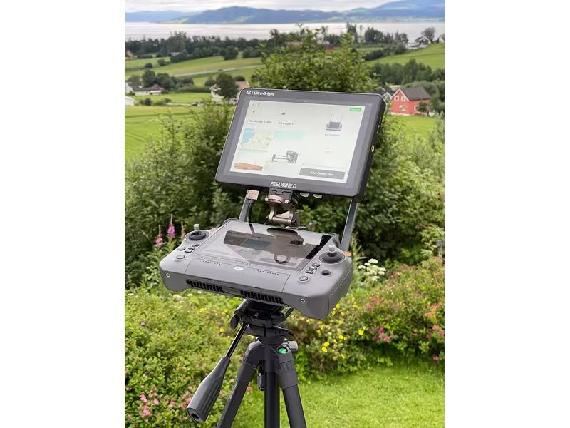 Ein LifThor RC PLUS Utility Mount II mit DJI Enterprise RC Plus-Controller steht inmitten grüner Hügel, Häuser und Wasser. Sein Bildschirm zeigt eine elegante Benutzeroberfläche, die zur ruhigen Szenerie passt.