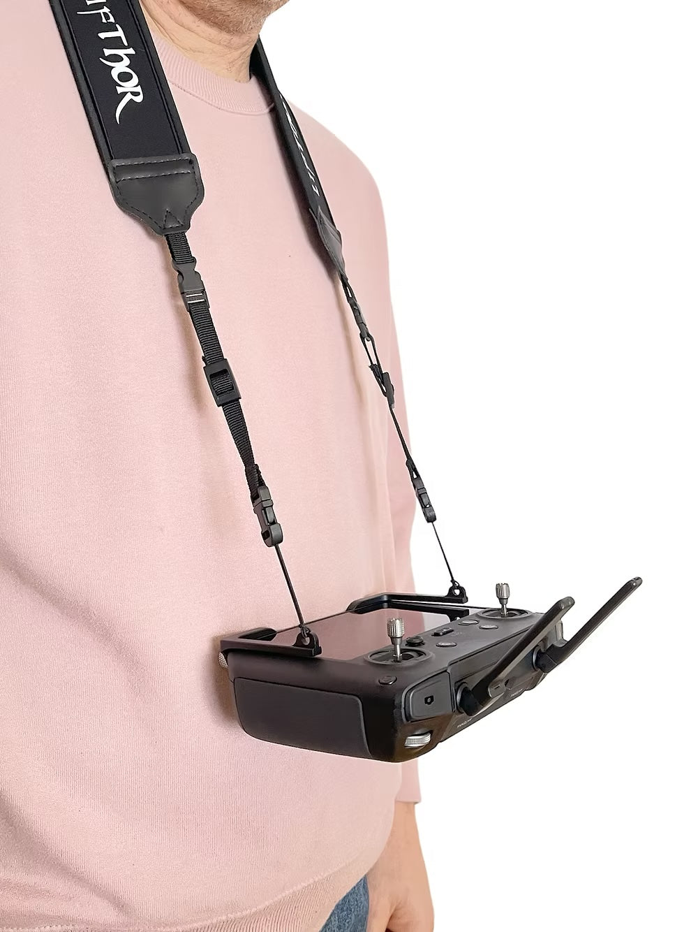 Eine Person in einem blassrosa Pullover hält einen schwarzen Smart Controller mit dem LifThor Sendergurt Claw PRO 2 für DJI RC Pro um den Hals. Die Fernbedienung verfügt über zwei Joysticks und eine Antenne. Auf dem Gurt ist der Markenname Lifthor zu sehen.