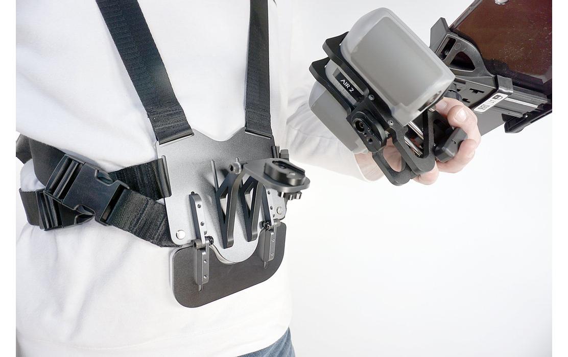 Eine Person, die einen schwarz-grauen LifThor Sendertragegurt StrapThor PRO trägt, bedient vor einem schlichten weißen Hintergrund ein Kamera-Ausrüstungen-Montagesystem mit einem großen Objektiv.