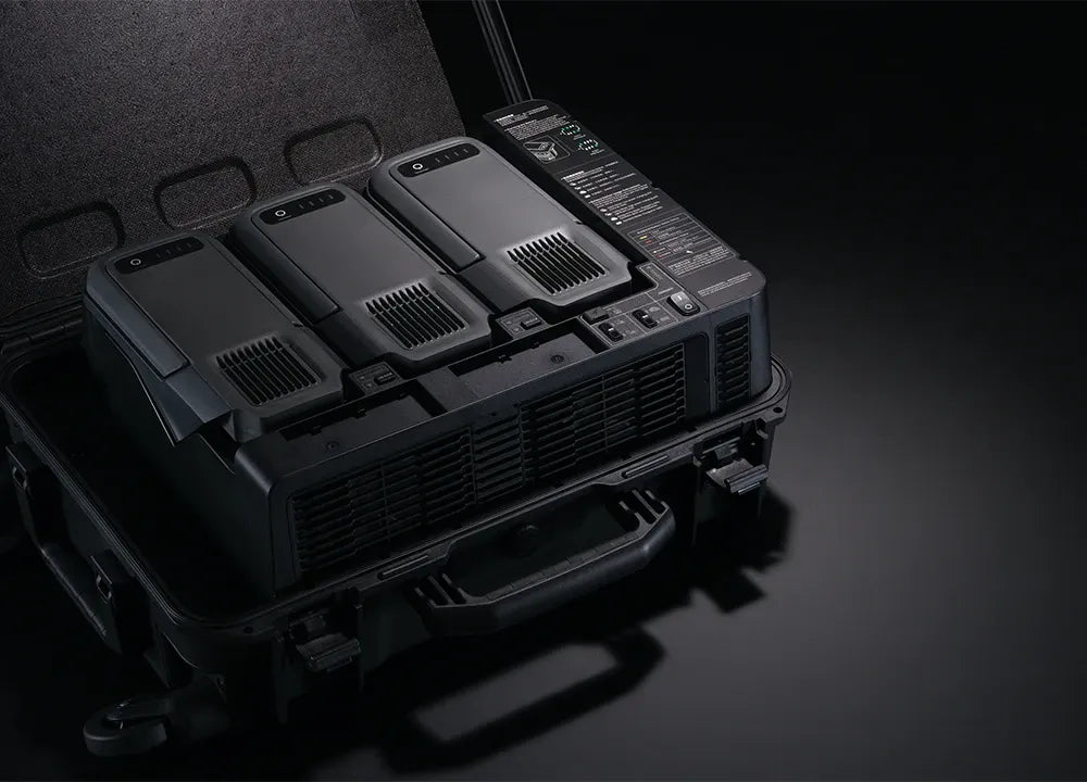 Die DJI BS100 Akkuladestation von DJI Enterprise verwaltet effizient vier große, schwarze TB100 Intelligent Flight Akkus mit Kontrollknöpfen und Anzeigeleuchten, ideal für die Matrice 400 RTK. Die Tragetasche hält die Akkus für den einfachen Transport organisiert.