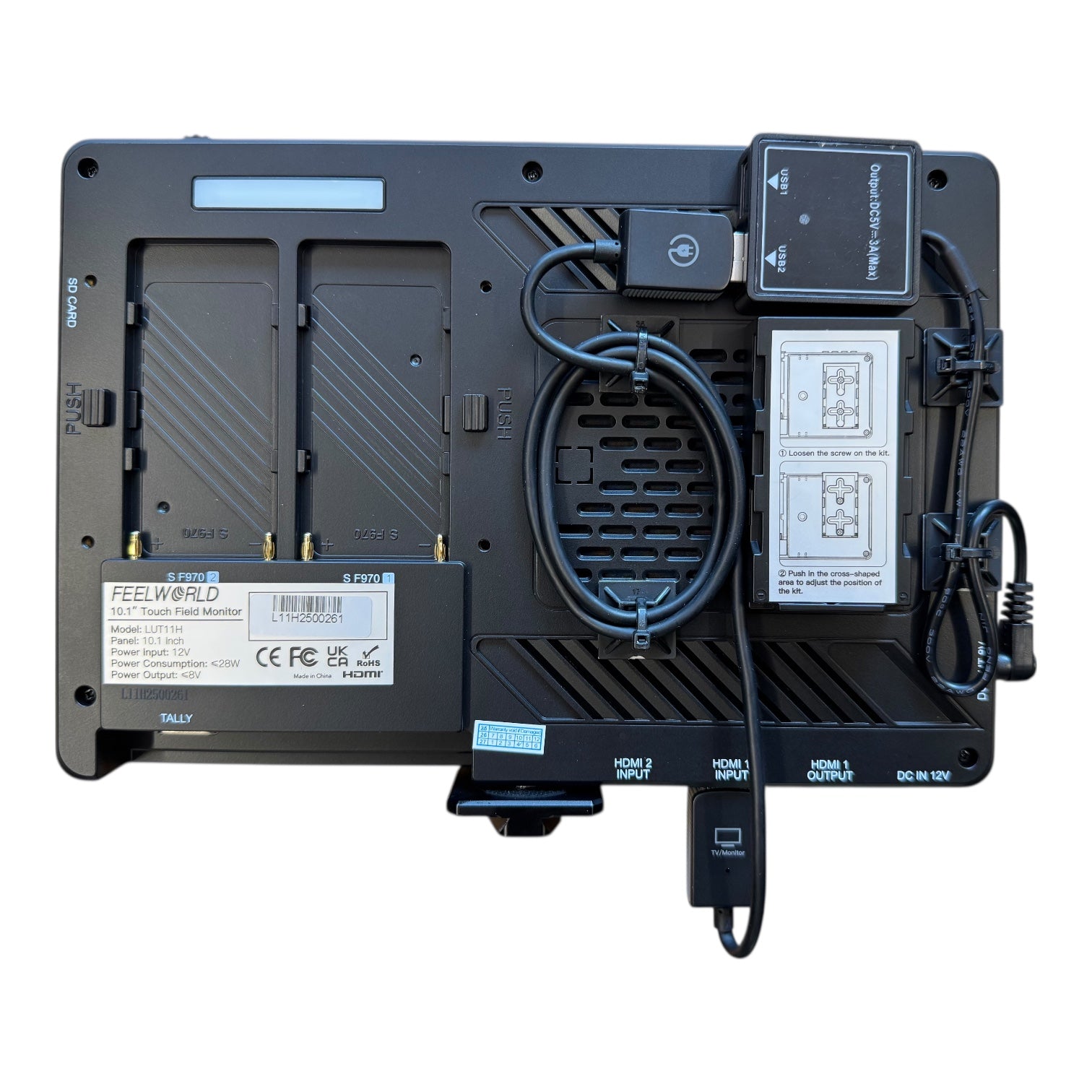 Rückansicht des CIELOTEC Aufwand Montage - Bildübertragung / Schnellverschlusssystem an Monitor, mit zwei Akkuschächten, HDMI-Anschlüssen, DC-Eingang und einem Spiralkabel mit Spannungswandler-Adapter vor weißem Hintergrund.