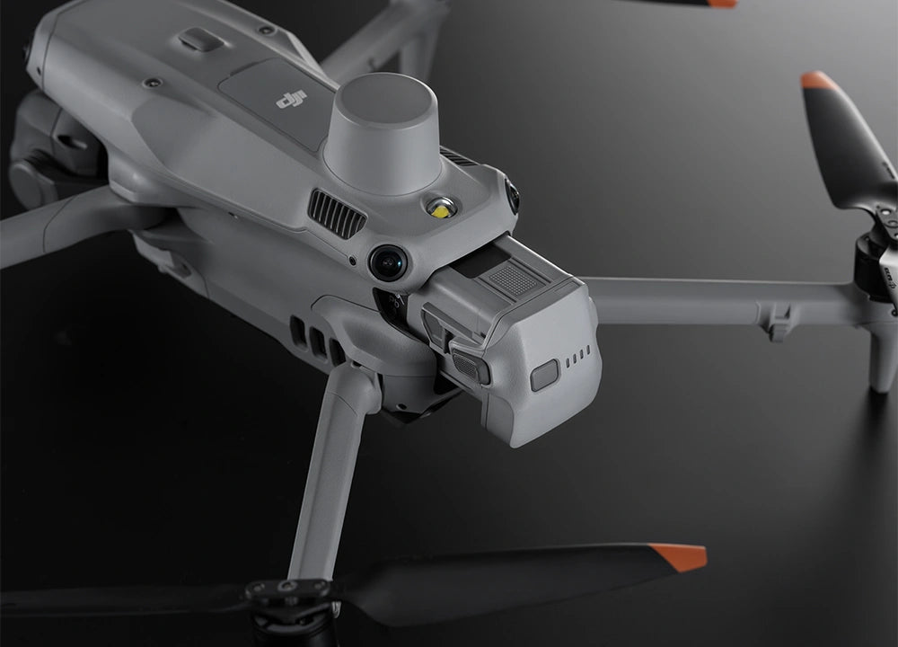 Eine graue DJI Matrice 4 Drohne mit Frontkamera und Topsensoren liegt auf einem dunklen Untergrund. Ihr kompaktes Design umfasst gefaltete Propeller mit orangefarbenen Spitzen. Ausgestattet mit einem DJI Enterprise Hochleistungsakku verspricht sie beeindruckende Flugzeiten.