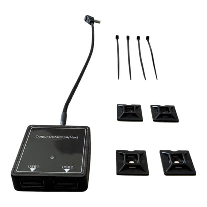 Der CIELOTEC 2-fach USB-A Spannungswandler (5V-3A, 5521 Buchse auf 2x USB-A) in schwarz enthält ein kurzes Kabel, zwei Anschlüsse, vier Kabelbinder und vier selbstklebende Kabelhalterungen, alles sauber auf weißem Hintergrund dargestellt.