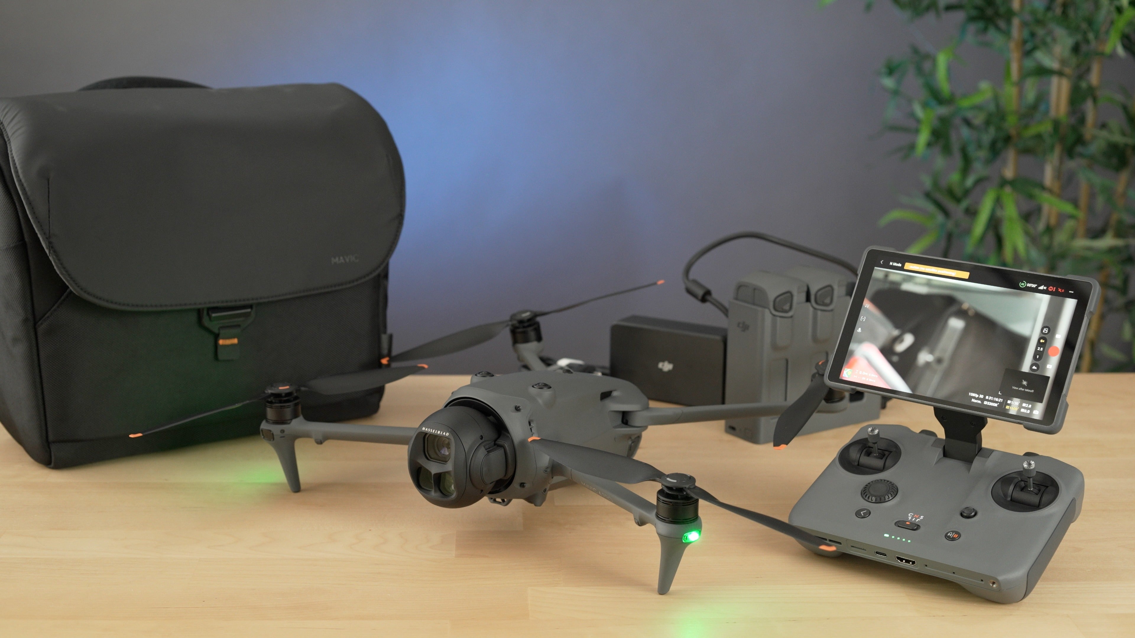 Eine DJI Mavic 4 Pro 512GB Creator Combo von DJI Consumer liegt auf einem Holztisch mit RC Pro 2 Controller, zwei Akkus, schwarzer Tasche und einer Blattpflanze - perfekt, um atemberaubende 100MP Hasselblad Fotos und 6K HDR Videos mit bis zu 51 Minuten Flugzeit aufzunehmen.