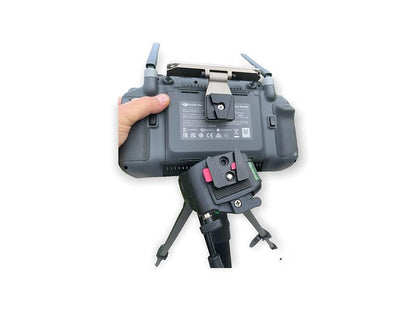 Eine Hand greift eine LifThor Stativhalterung für die DJI RC Pro Plus-Fernbedienung mit faltbaren Antennen und Aluminium-Akzenten. Sie ist auf einem verstellbaren Stativ montiert und auf der Rückseite mit Zertifizierungslogos versehen.
