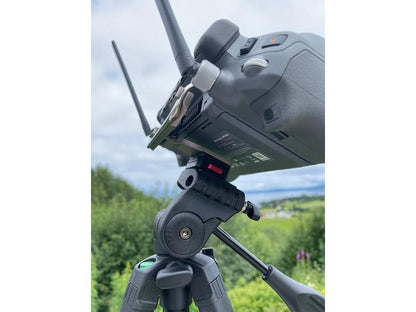 Nahaufnahme einer LifThor Stativhalterung für die DJI RC Pro Plus-Fernbedienung, montiert auf einem Aluminiumständer. Das Gerät mit Doppelantenne und mehreren Tasten ist vor üppigem Grün und einem bewölkten Himmel zu sehen.
