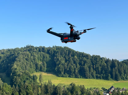 Eine gebrauchte DJI Matrice 3TD von DJI Enterprise (NP: Fr. 11'000.- / VP: Fr. 5'500.-) in sehr gutem Zustand, ideal für Rettungseinsätze mit ihrer robusten IP54-Einstufung, fliegt über eine grüne Landschaft an einem klaren, sonnigen Tag.