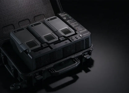 Die DJI BS100 Akkuladestation von DJI Enterprise verwaltet effizient vier große, schwarze TB100 Intelligent Flight Akkus mit Kontrollknöpfen und Anzeigeleuchten, ideal für die Matrice 400 RTK. Die Tragetasche hält die Akkus für den einfachen Transport organisiert.