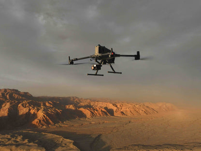 Ein DJI Enterprise Multikopter Matrice 400 RTK (M400 RTK) (EU/C3) mit Kamera schwebt über einem weiten, trockenen Wüstengebiet mit zerklüfteten Hügeln unter einem dramatischen, bewölkten Himmel.